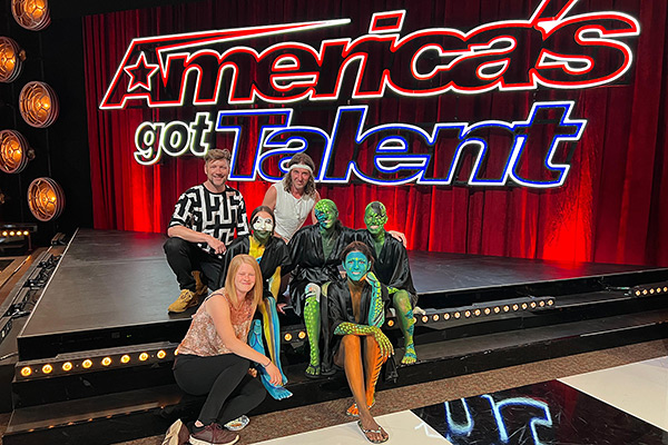 Gruppe von Künstlern und Models mit Bodypainting in Grün- und Orangetönen vor der großen „America’s Got Talent“-Bühne.