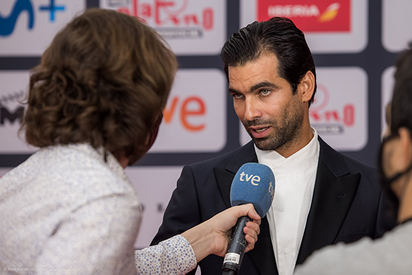 Ein Mann im Anzug wird auf dem roten Teppich bei den Platino Awards von einem TVE-Reporter mit Mikrofon interviewt.