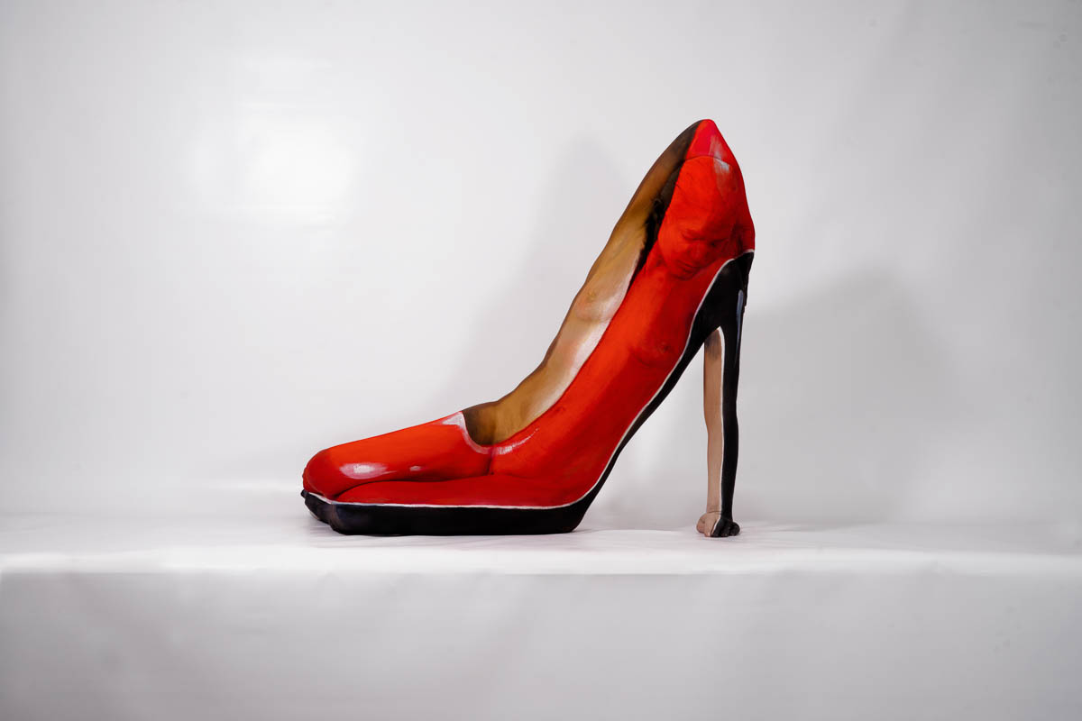 Optische Illusion eines roten High Heels, geformt aus mehreren bemalten menschlichen Körpern, die so arrangiert sind, dass sie wie ein Schuh wirken.