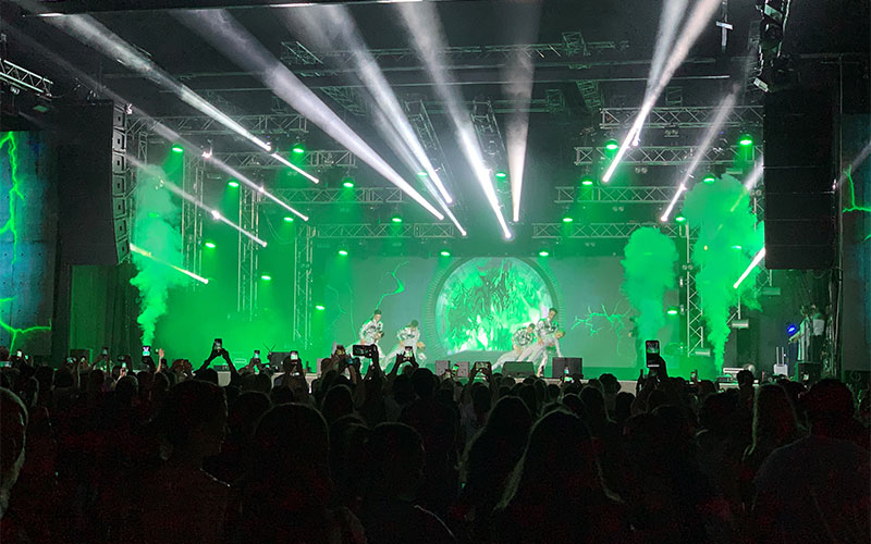 Preisverleihung beim Bodypainting-Festival: Künstler und Models in spektakulären, farbenfrohen Bodypainting-Kostümen stehen jubelnd auf der Bühne, während im Hintergrund ein Feuerwerk auf der Leinwand zu sehen ist und das Publikum applaudiert.