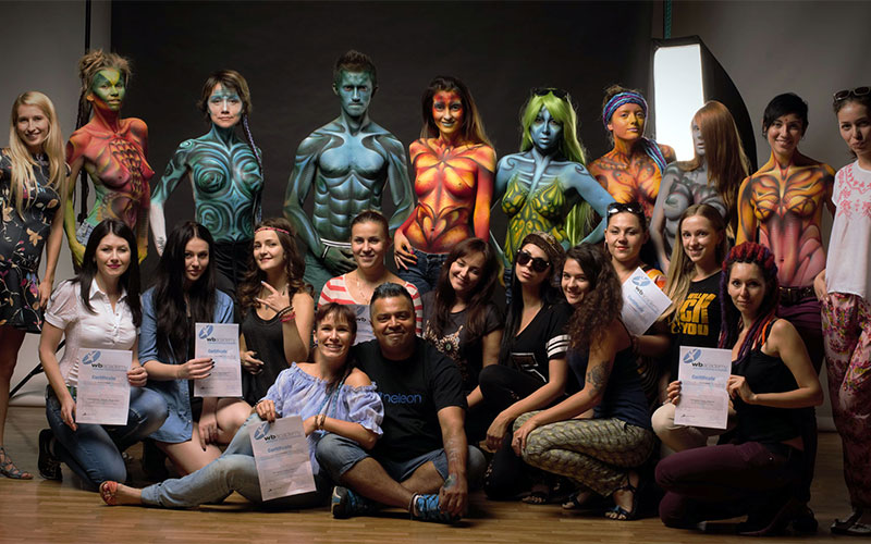 Gruppenfoto bei einem Bodypainting-Wettbewerb: Künstler und Models mit fantasievollen, farbenprächtigen Bodypaintings posieren gemeinsam auf der Bühne, während Jury und Gäste davor stehen
